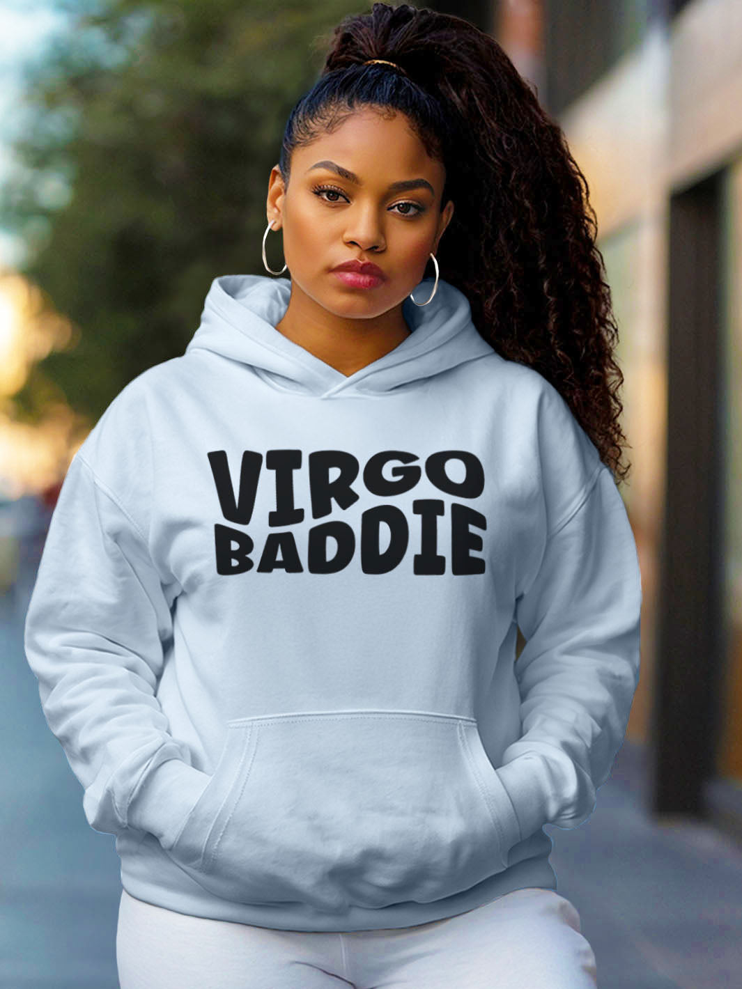 Woman wearing a light blue color custom graphic hoodie with bold black text design artwork that reads “VIRGO BADDIE” in large, playful bubble style block letters.